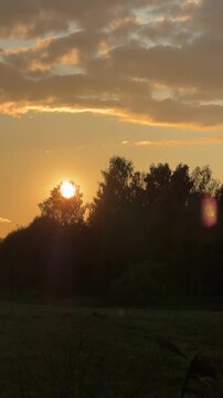 Sunset illuminates a peaceful landscape with silhouetted trees and a bright sun, creating a serene atmosphere in the evening sky