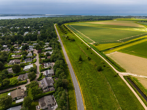 High angle wide horizontal aerial drone photograph of coastal road, grass dike, holiday park, polder fields, and North Sea horizon in Kamperland, Zeeland, Netherlands on sunny summer day