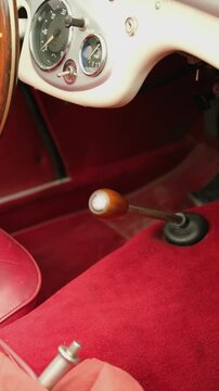 Luxurious classic car interior with wooden gear knob, chrome gauges and plush red carpet evoking nostalgic elegance. Vertical video