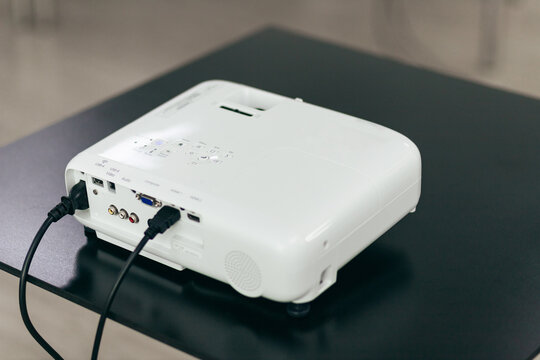 White Projector With Connected Cables On Black Desk. Rear View Of Electronic Presentation Equipment Ready For Use.