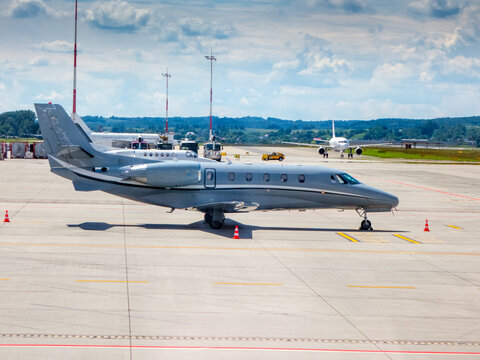 Business jet, painted in a silver-grey livery at the tarmac. A white airplane in the background. Midsize, twin-engine corporate jet. grey exterior paint scheme with rear-mounted turbofan engines. 