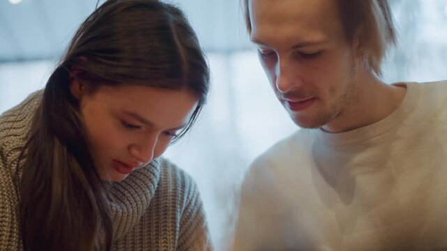 Close up of two people woman and man looking down at something together in soft lighting. scene shows them focused on unseen object or screen with natural expressions set against blurred