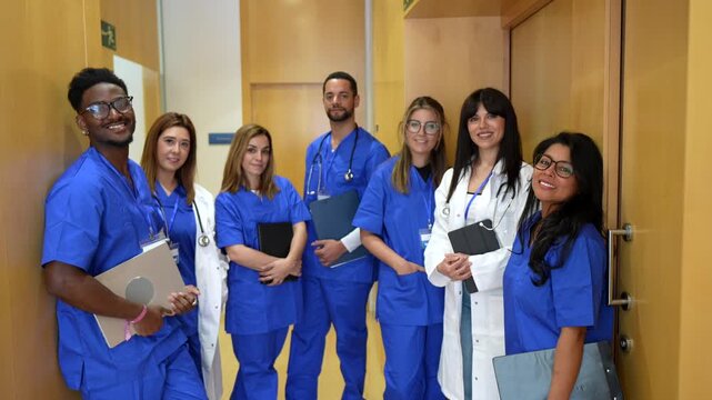 Professional group of multicultural medical students and doctors standing together in a hospital corridor, smiling at the camera, ready for their clinical practice or internship