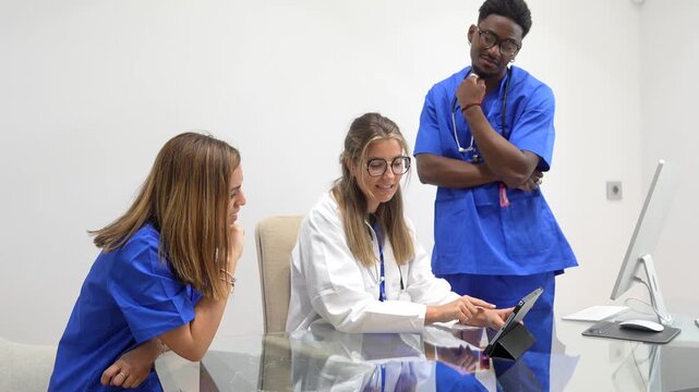 Three multicultural medical professionals, a doctor and two nurses, collaborating in a modern clinic office, analyzing patient data and diagnosis on a digital tablet and computer