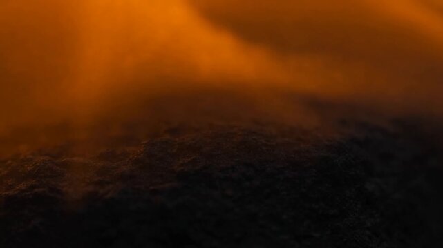 Dark textured surface beneath glowing orange haze in an abstract shadowy setting