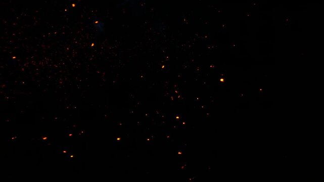 Glowing orange embers and faint smoke suspended against a dark black background