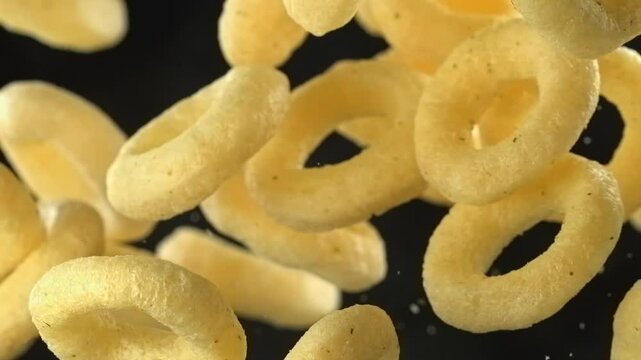 Crunchy cheese flavored onion rings falling in super slow motion on black background