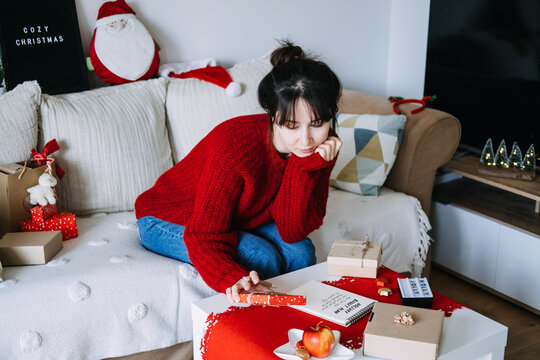 Woman writes in notebook with HOLIDAY BUDGET PLAN on table beside gifts and COZY CHRISTMAS sign. Saving money for christmas, financial goal setting holiday, christmas expense management