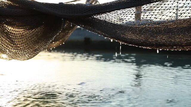 Fishing net suspended over water with droplets hanging above rippled surface