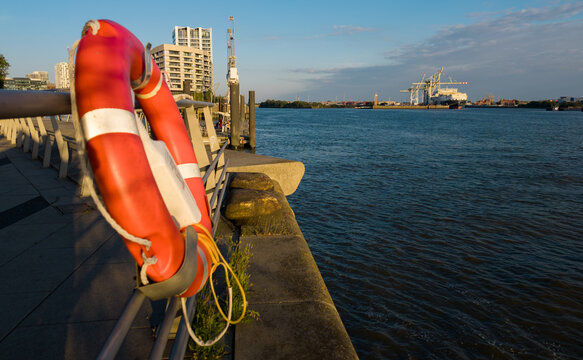 Orange lifebuoy hanging on a railing along the Elbe river waterfront, Hamburg harbor in background