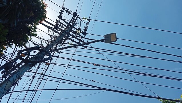 Low Angle View of Tangled Power Lines and LED Street Light on Concrete Utility Pole Against Blue Sky