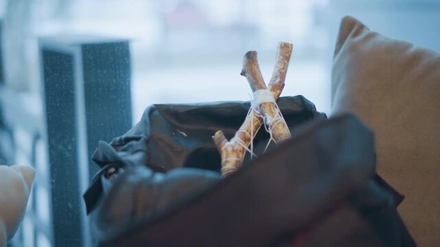 Close up of tied bundle of sticks resting in open black bag with soft lighting and out of focus background. scene features warm indoor tones natural textures from wooden stick bundles string