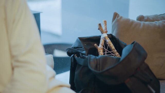Close up of small wooden teepee structure tied with string inside open black bag. scene is set in soft indoor lighting featuring neutral tones and minimal background details to emphasize