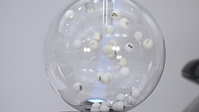 Numbered lottery balls spinning inside clear sphere, slow motion