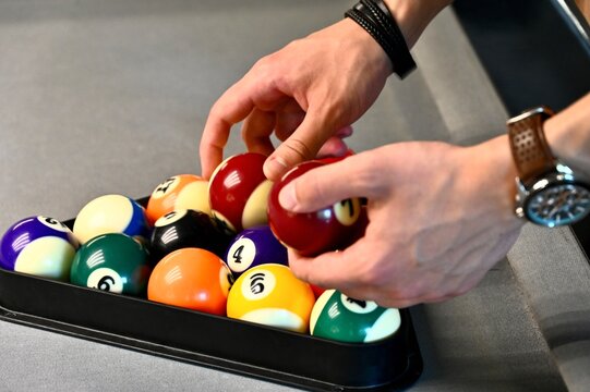 capturing a person's hands as they arrange colorful numbered billiard balls inside a triangle rack on a pool table.