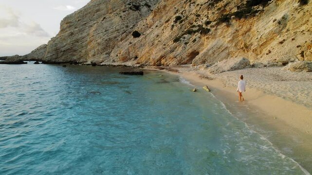 Woman walks along tranquil turquoise shore of remote Kefalonia beach at dusk