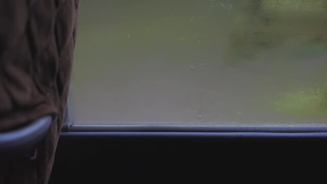 Point of view from inside moving vehicle, looking out steamy foggy window with blurred, green background during cold day outdoors with condensation on glass of bus or van during a ride on highway