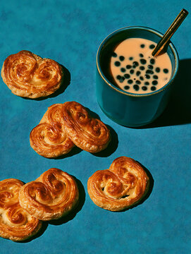 A French Palmier pastry placed next to a cup of milk tea