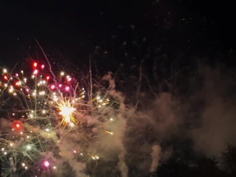 Bright golden and green fireworks exploding in the dark night sky during a festive celebration.