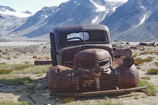 Old, rusty car in a junkyard with a view of mountains and blue sky in the background, remains from the Second World War, Ikateq 2, East Greenland, Denmark
