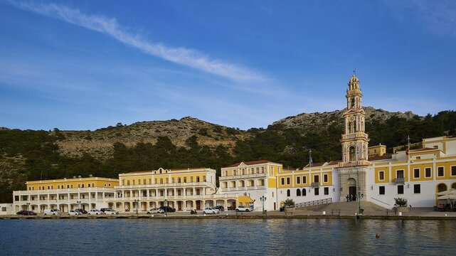 Large monastery complex along the coastline with yellow facades in front of a forest view, Holy Week, Panormitis Bay, Panormitis Monastery, Symi, Dodecanese, Greek Islands, Greece