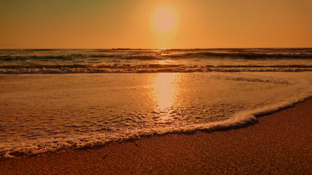 Low angle view of ocean waves washing onto a sandy beach at sunset