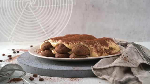 Delicious homemade tiramisu cake served on a plate with cocoa powder and coffee beans on a kitchen table