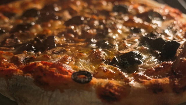 Close-up of a freshly baked pizza inside a hot oven with melted cheese bubbling and dark olives
