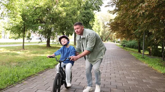 Father teaching his son to ride bicycle outdoors, camera moving backwards. Child safety