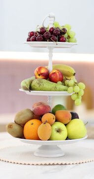 Fruit stand filled with mix of fresh juicy fruits on white marble table in kitchen, camera moving in