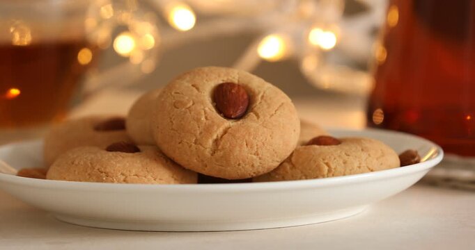 Tasty cookies with almonds and tea on light table against blurred lights, closeup. Camera moving right