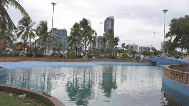 tropical coconut palm trees bending in strong sea winds in front of modern coastal skyscrapers and high rise condominiums viewed from 'koh loi' park, thailand