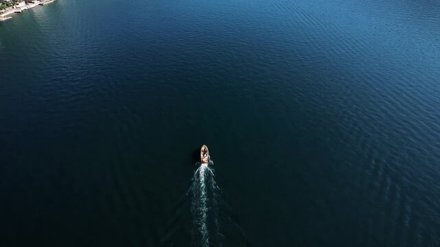 Single boat traverses expansive shadowy ocean. Lone ship moving through deep mysterious waters with symmetrical trail