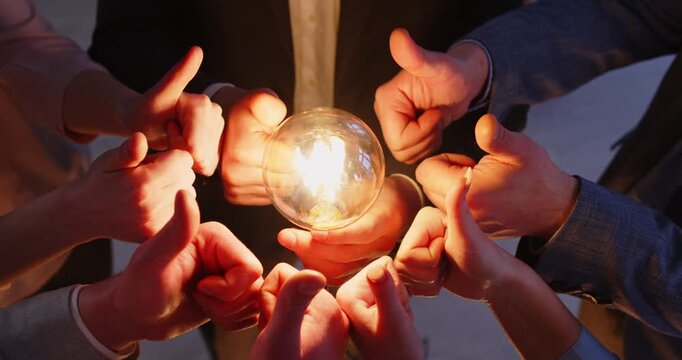 Business people holding illuminated light bulbs, keeping thumbs up, sharing creative innovative ideas, brainstorming in office, have common interests work as team. Brainstormig concept