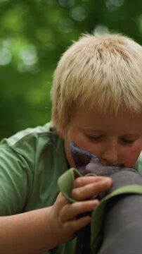 Blonde haired kid holds onto large furry canine. Close up shows child adjusting hold near back of canine head. Setting is open space filled with soft focus green plant life