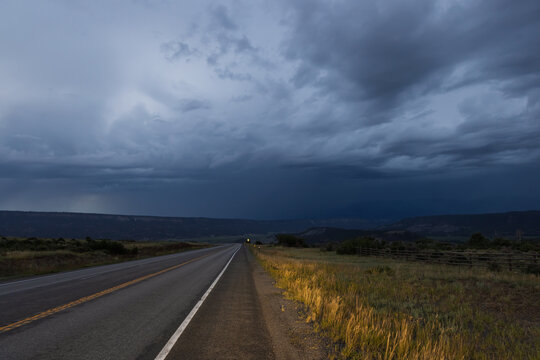 Empty highway leading into storm clouds over countryside