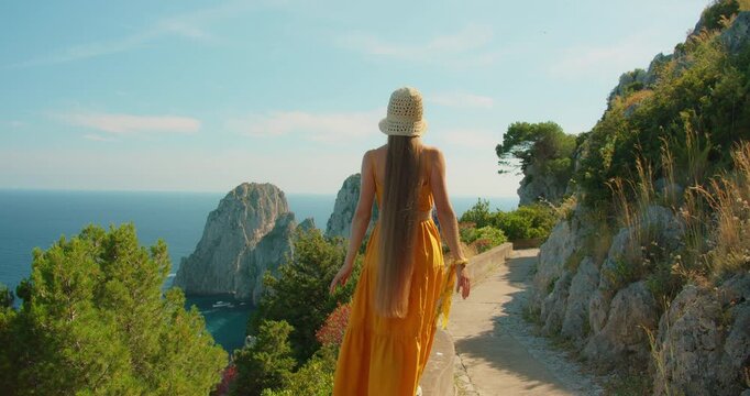 Woman walking coastal path with Faraglioni cliffs ahead in Capri Island, Italy