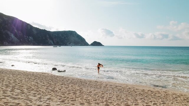 Woman walking on sandy beach near turquoise sea in sunny summer day in Kefalonia