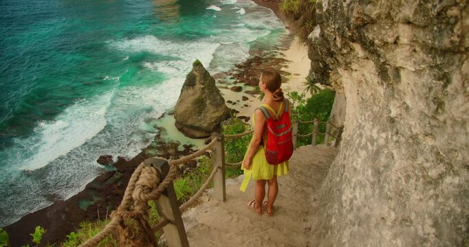 Woman stands on steep stairs looking at beautiful beach and turquoise sea water in Nusa Penida Bali