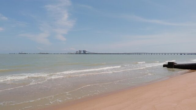 4K slow-motion panning shot of Pantai Puteri beach, Melaka, panning right from the distant refinery over the Strait of Malacca to coastal outfall pipes and resting boats.