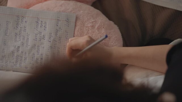 High-angle view of both hands writing dense handwritten notes in open lined notebook, pen moving across page while fingers steady paper in warm indoor light with soft blur and calm focus