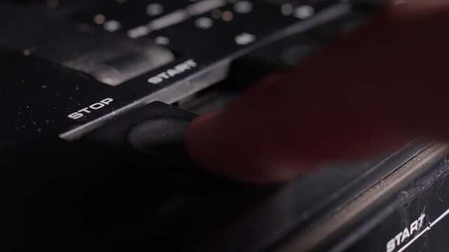 Finger presses stop button on vintage analog audio equipment, macro closeup