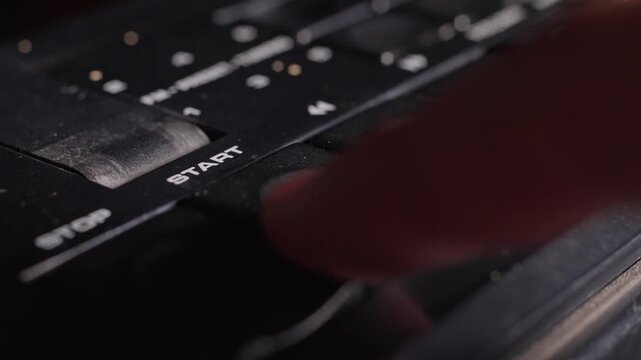 Close detail of vintage analog audio controls with black start and stop buttons on analog equipment, finger presses down play button