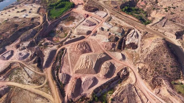 Massive clay mining fields with excavated pits, dirt roads and exposed earth formations, aerial panoramic overview of stockpiles with grey and brown textures