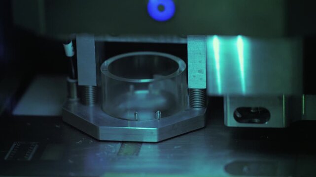A macro shot of industrial precision machinery featuring a transparent cylindrical component mounted on a metal base under cool blue lighting.