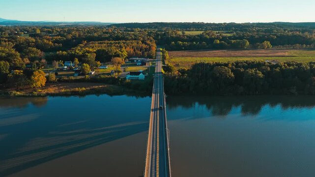 Road bridge crosses a broad river toward autumn countryside near Ozark, Arkansas, aerial symmetrical pullback