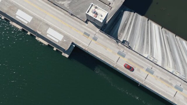 Top-down aerial of a red car crossing the roadway over Bull Shoals Dam in Arkansas, angled cross section tilting backward upward reveal to electrical substation