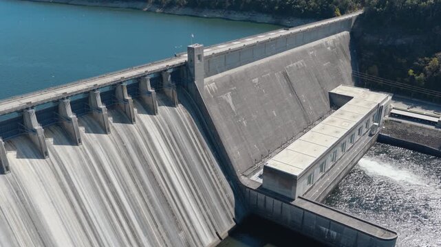 Concrete Bull Shoals Dam and spillway border blue reservoir water in Arkansas, aerial angled tracking pullback over white grey concrete