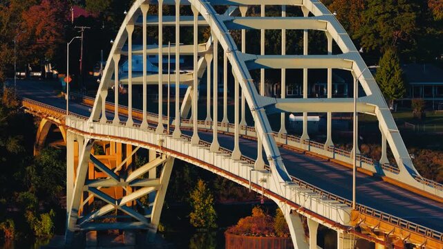 White steel arch bridge curves above a roadway among autumn trees in Ozark, Arkansas, aerial telephoto slow approach