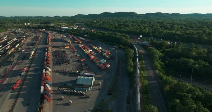Large freight intermodal rail yard with rows of containers and tracks in Nashville, Tennessee, aerial orbit at sunset
